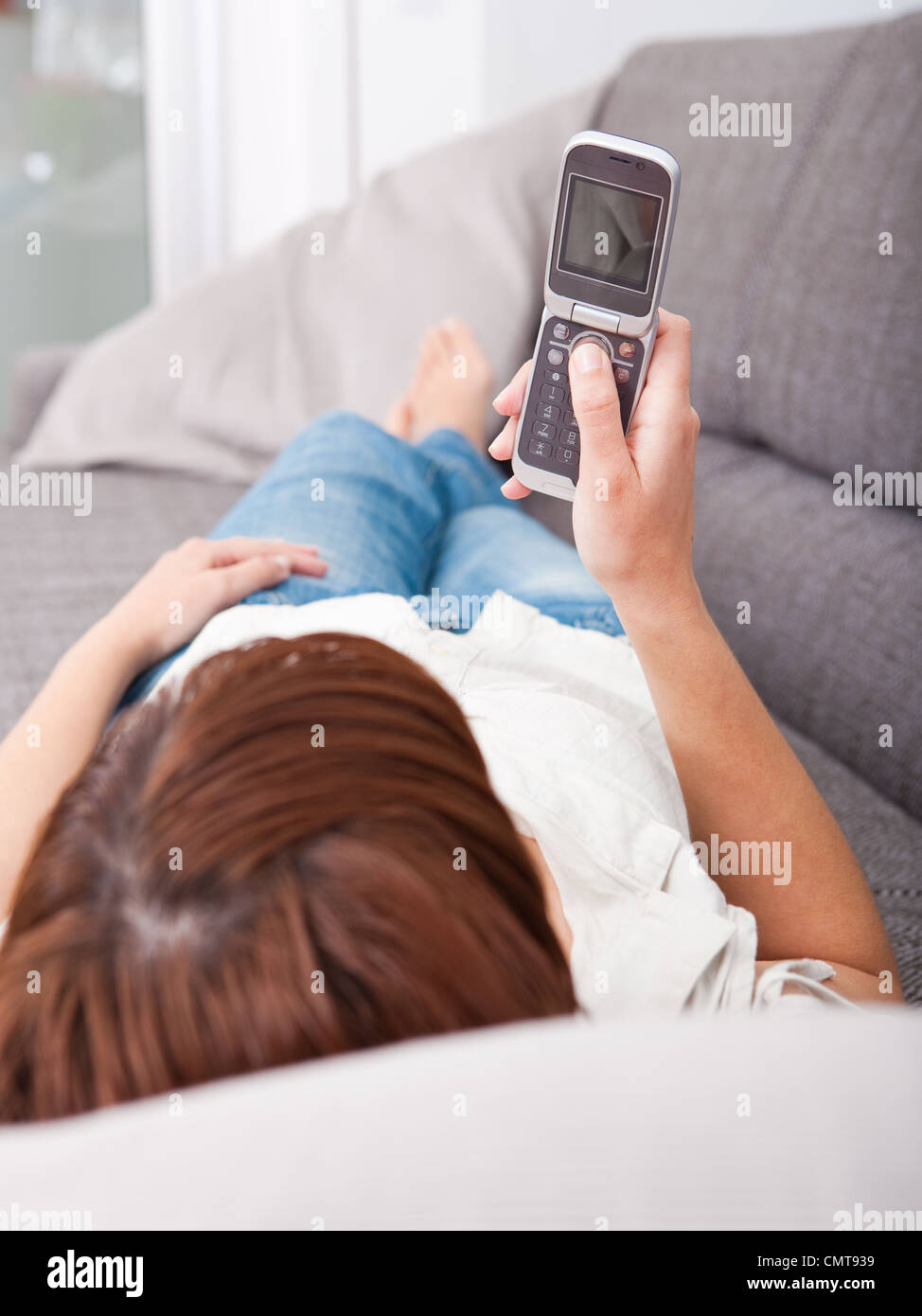 Porträt einer schönen Frau auf Sofa hält ein Handy und ein Sms-Versand Stockfoto