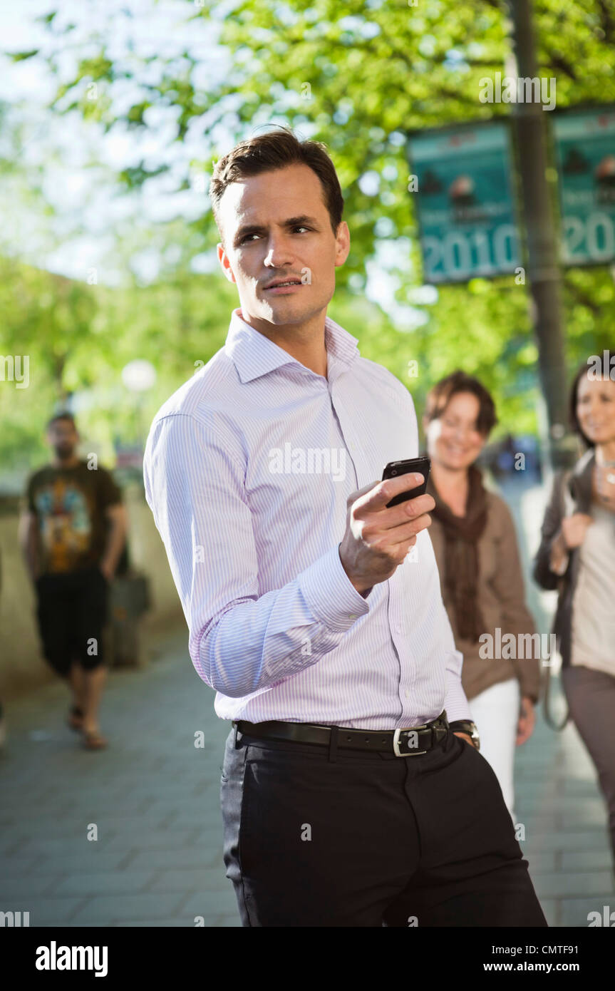 Mann hält Handy mit Menschen im Hintergrund Stockfoto