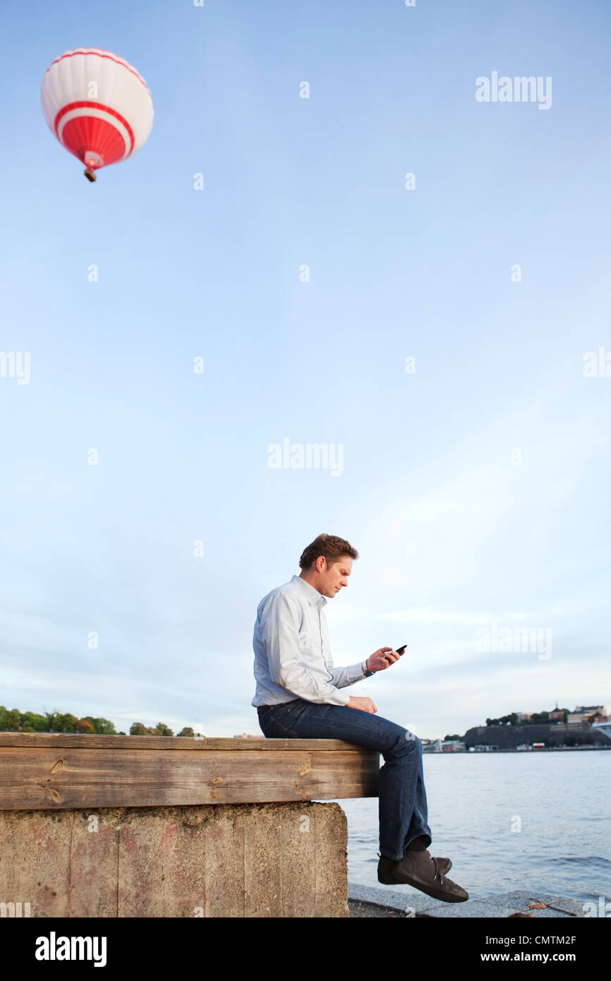 Mann sitzt am Rand mit Handy in der hand Stockfoto