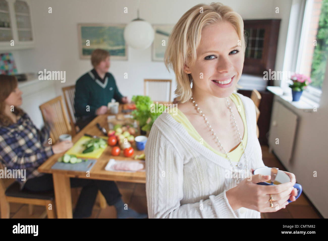 Lächelnde Frau hält Cup mit Menschen im Hintergrund Stockfoto