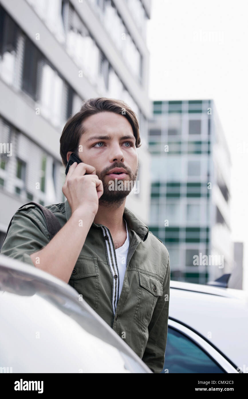 Deutschland, Köln, junger Mann am Telefon in der Nähe von Auto Stockfoto