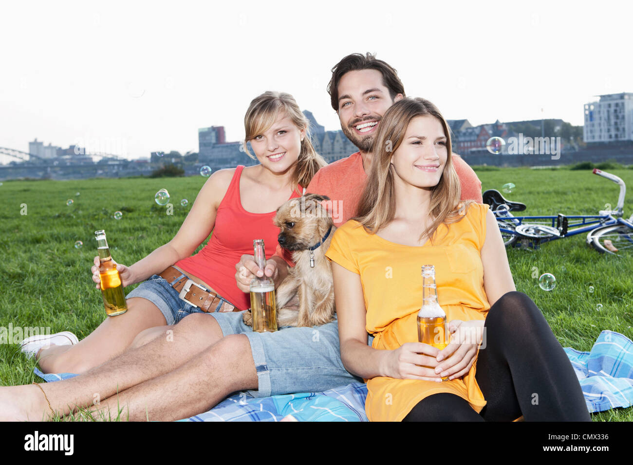 Deutschland, Köln, junger Mann und Frau mit Hund und Bier Flasche Gras, Lächeln Stockfoto