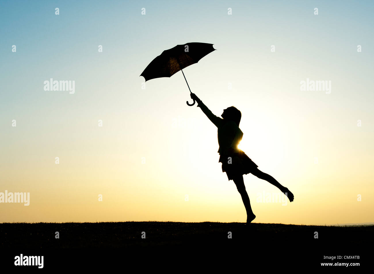 Junges Mädchen springen mit einem Regenschirm bei Sonnenuntergang. Silhouette Stockfoto