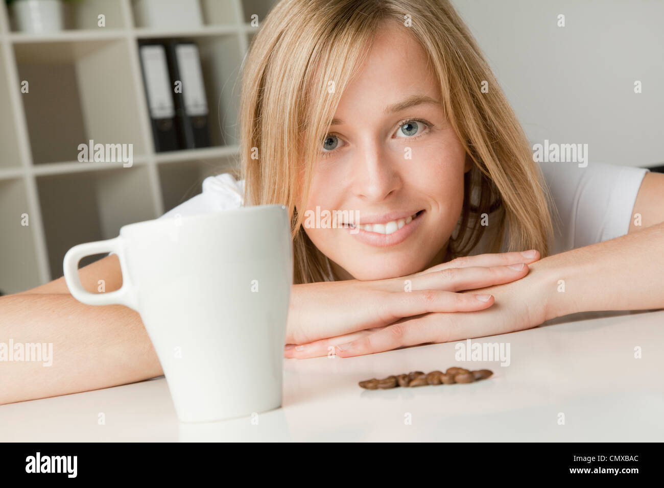 Junge Frau mit Kaffeetasse und Bohnen, Lächeln, Porträt Stockfoto