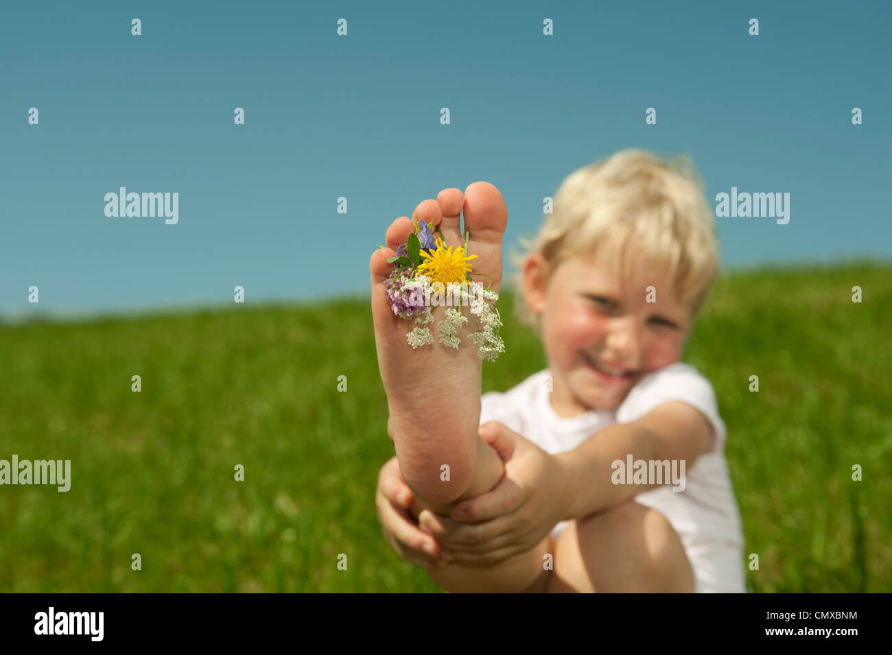 Deutschland, Bayern, Mädchen spielen mit Blumen zwischen den Zehen auf dem Rasen, Lächeln, Porträt Stockfoto