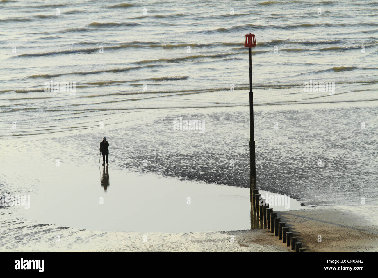 Eine einsame Figur spiegelt sich im Wasser am Strand von Eastbourne, East Sussex, England Stockfoto