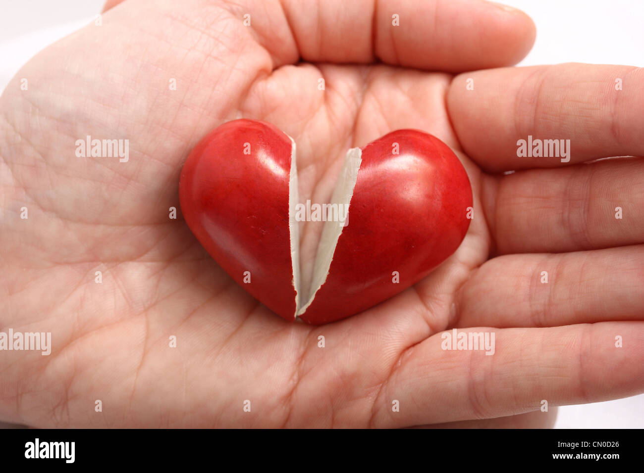 Symbolisches Bild, Herz-Kreislauferkrankungen, Herzinfarkt, Schutz, Prävention, Kardiologie. Hände halten ein gebrochenes rotes Herz in 2 Stücke. Stockfoto