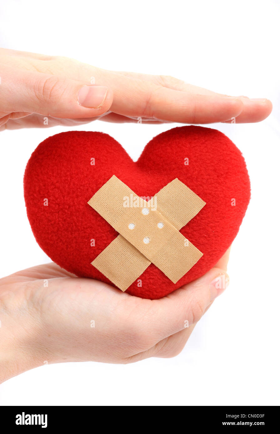 Symbolisches Bild, Herz-Kreislauferkrankungen, Herzinfarkt, Schutz, Prävention, Kardiologie. Hände halten ein rotes Herz mit einem Pflaster. Stockfoto