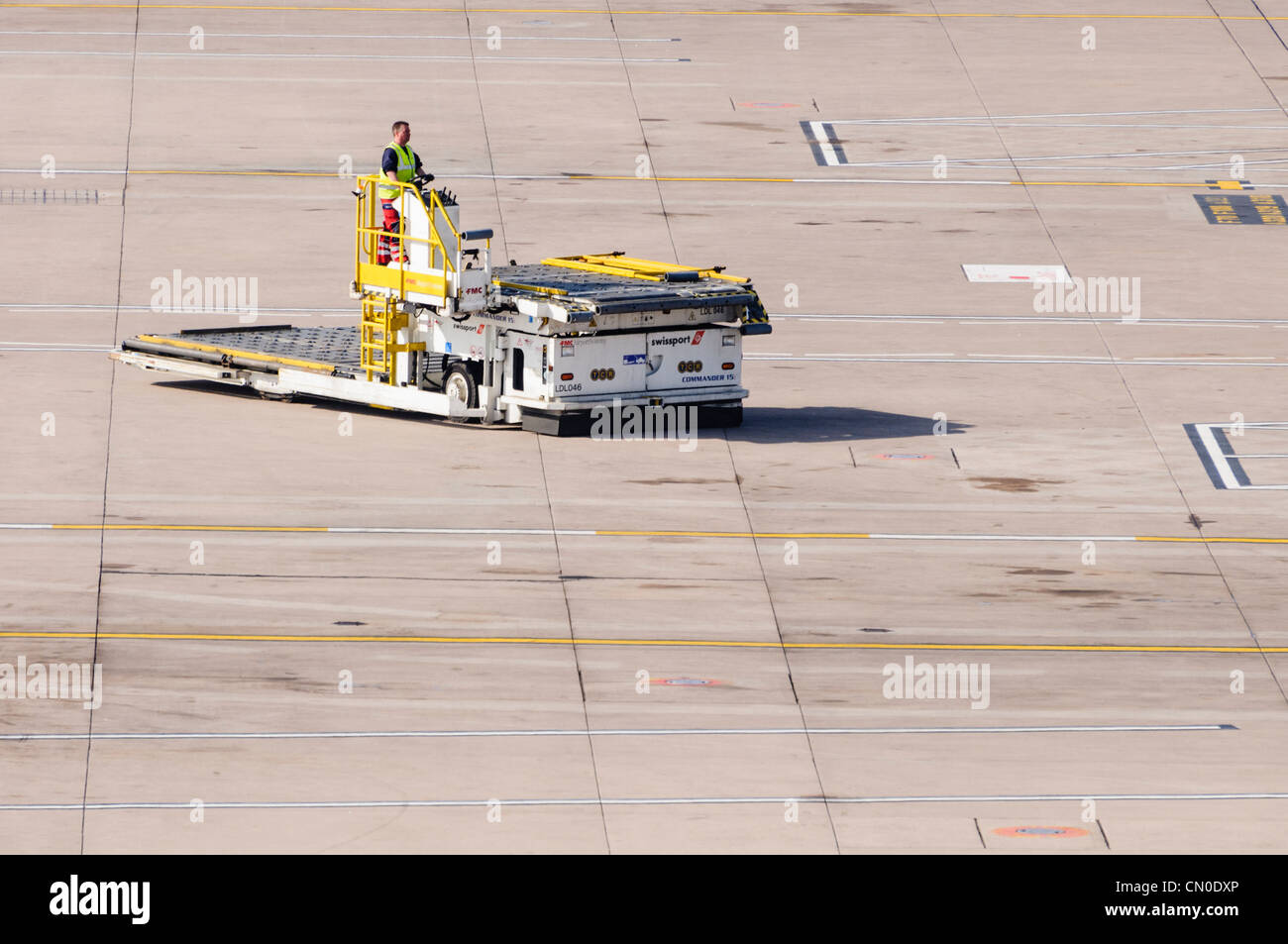 Flughafen-Container-Transporter getrieben über einem leeren Flughafen-Vorfeld Stockfoto