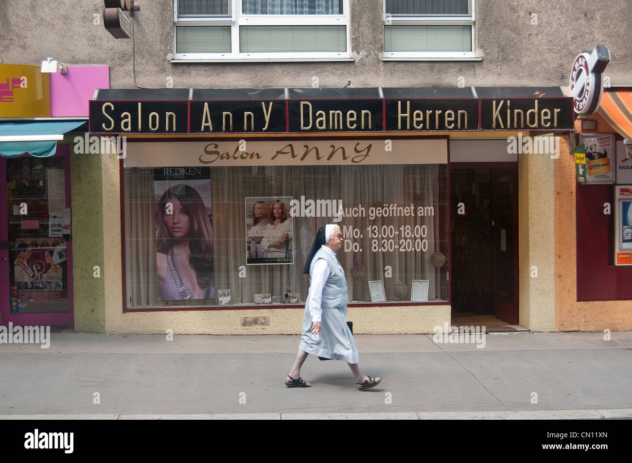 Eine Nonne geht eine Straße in einem Wiener Stadtteil entlang Vorbei an einem Friseursalon Stockfoto