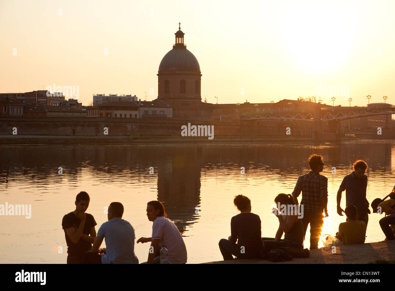 Leute sitzen am Ufer des La Garonne, wenn die Sonne untergeht in der Nähe von Dome De La Grave, Toulouse, Frankreich Stockfoto