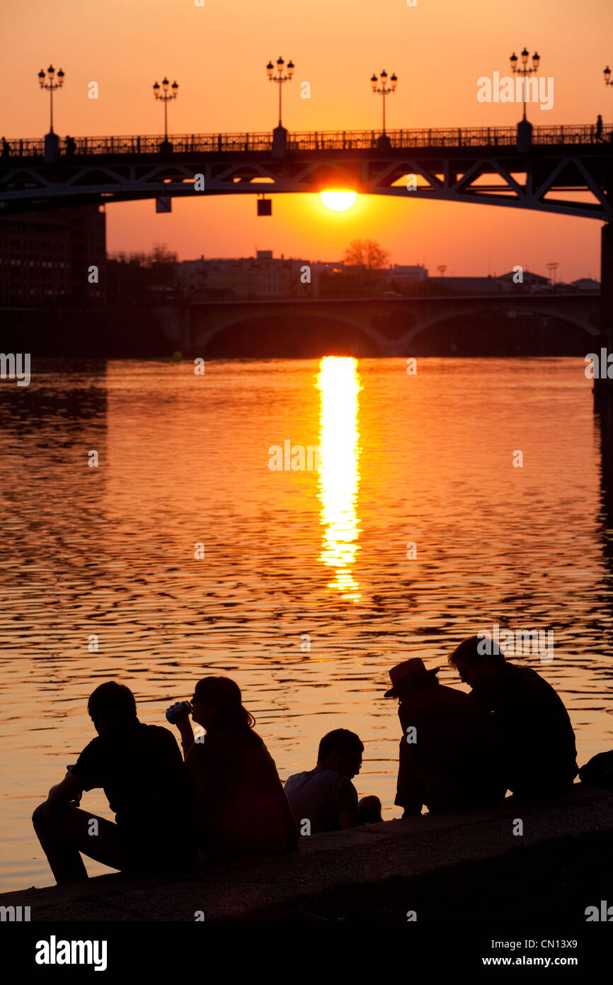 Französische Leute saßen an den Ufern des La Garonne den Sonnenuntergang hinter der Pont St. Pierre, Fluss Garonne, Toulouse, Frankreich Stockfoto