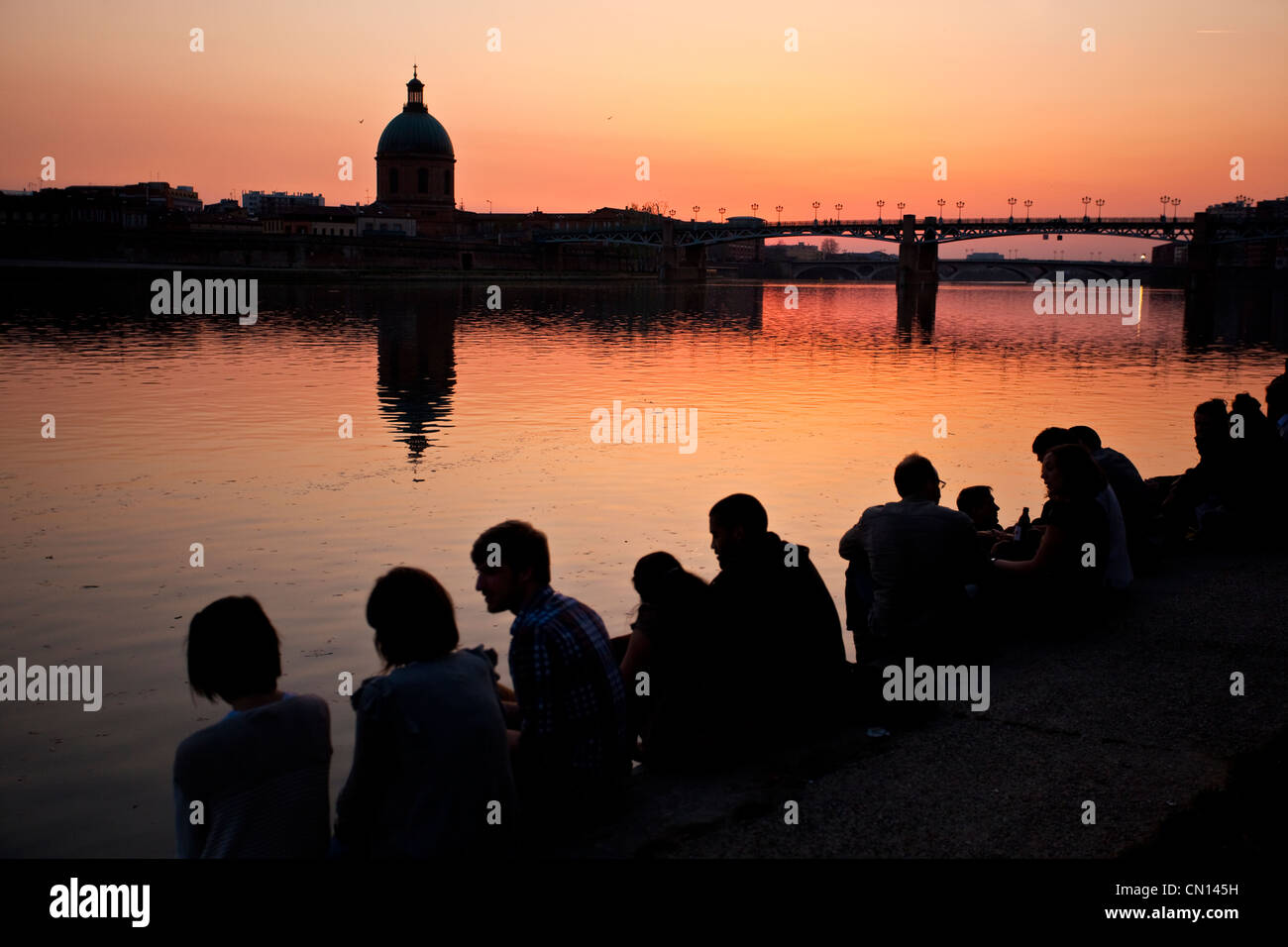 Leute sitzen am Ufer des La Garonne bei Sonnenuntergang mit Blick auf die Kuppel De La Grave und St-Pierre Brücke, Toulouse, Frankreich Stockfoto