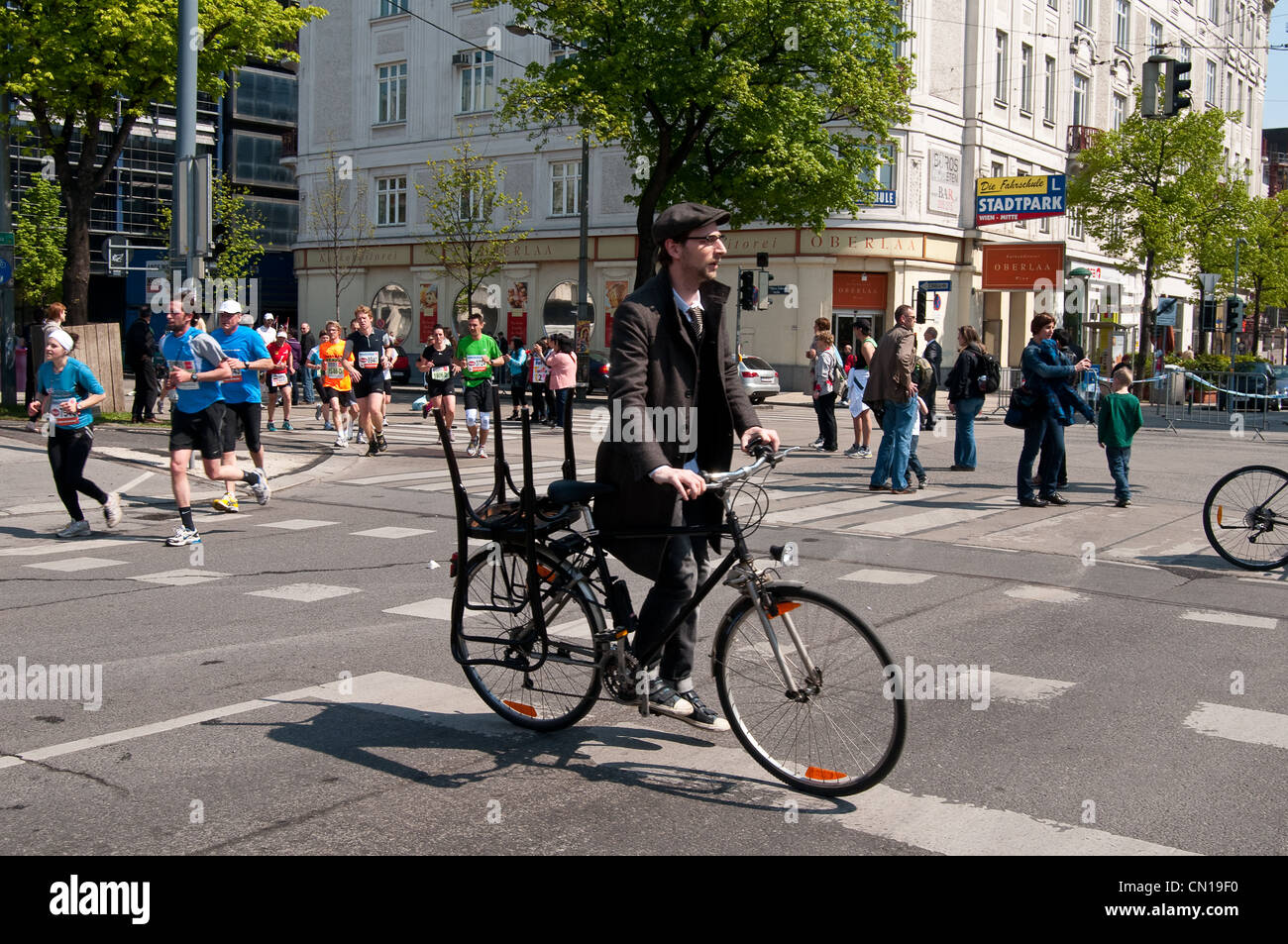 Ein Mann auf seinem Fahrrad mit einem Stuhl befestigt, während Jogger in Vienna City Marathon teilnehmen. Stockfoto