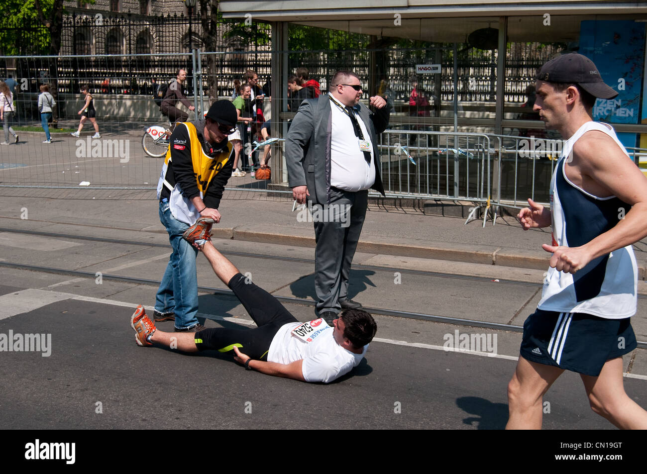 Ein Jogger macht eine Pause zu bekommen sein Bein erstreckte sich vom Steward beim Vienna City Marathon, während ein Wachmann blickt auf. Stockfoto