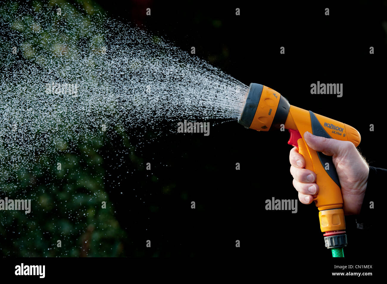 Gärtner Hand sprühen Wasser mit Gartenschlauch gegen einen dunklen Hintergrund. Großbritannien Stockfoto