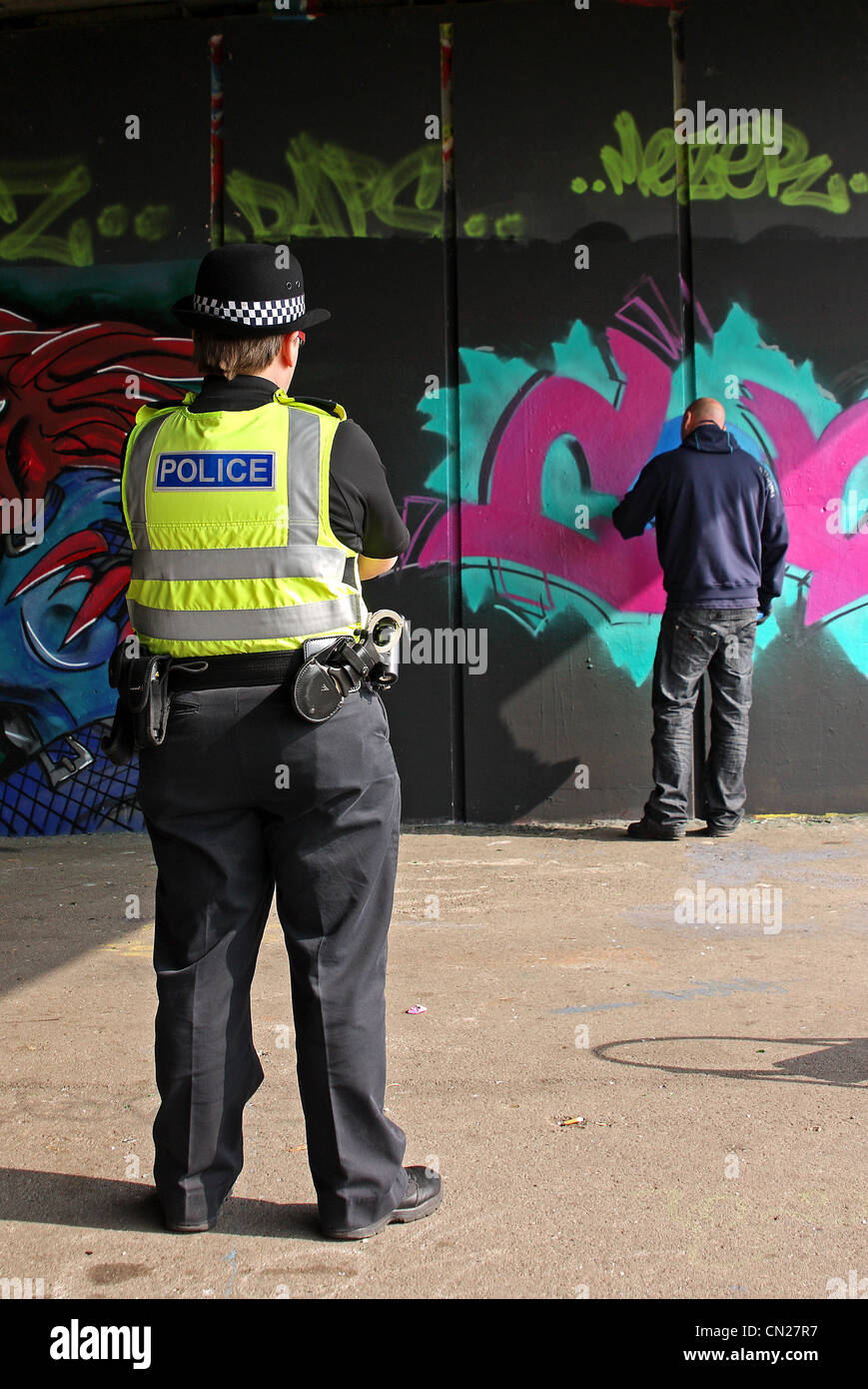 Graffiti-Künstler bei der Arbeit unter einer Straße von einem Polizisten beobachtet Stockfoto