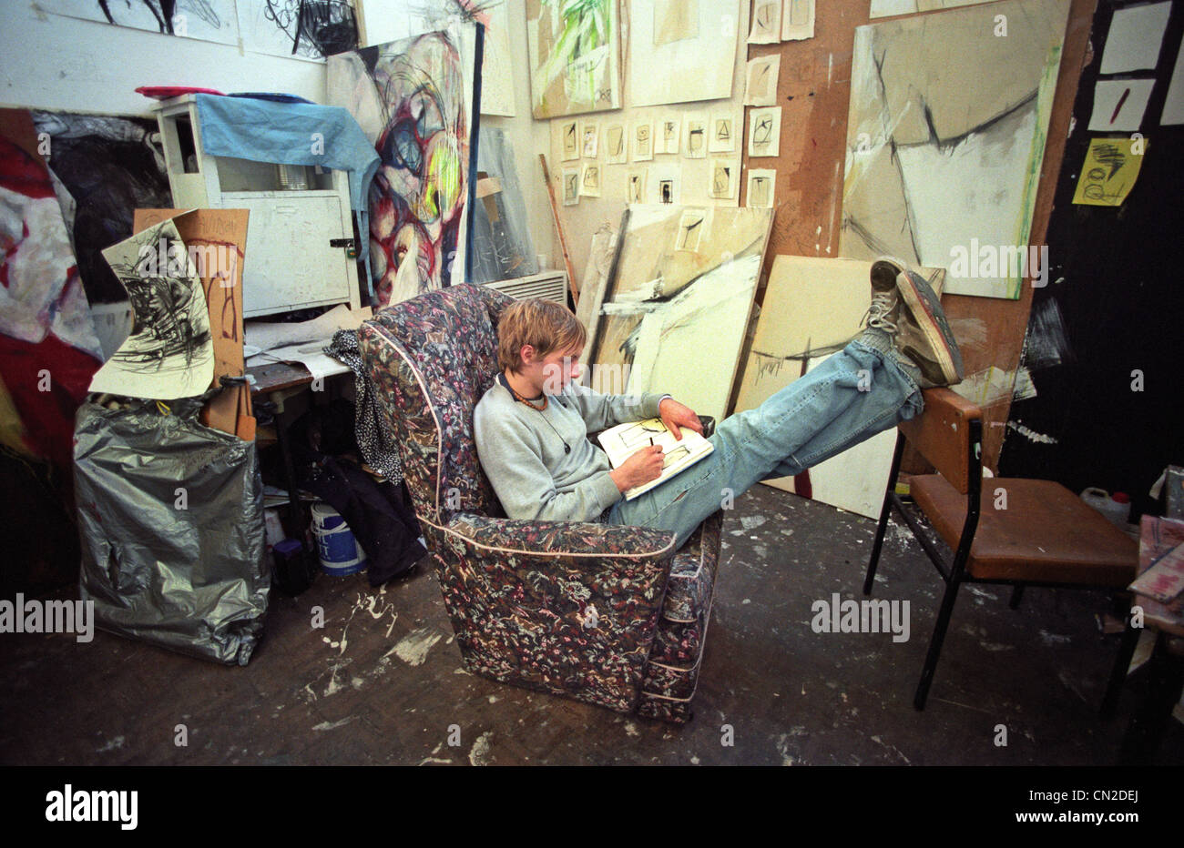 Junge männliche fein Kunststudentin mit Füßen im Atelier des Malers eine chaotische Stockfoto
