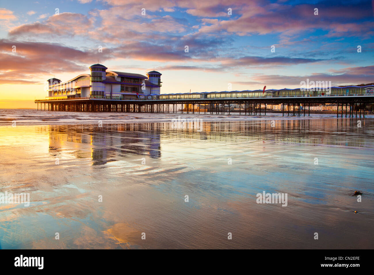 Sonnenuntergang über dem Grand Pier bei Weston-Super-Mare, Somerset, England, UK spiegelt sich in dem nassen Sand des Strandes bei Flut. Stockfoto