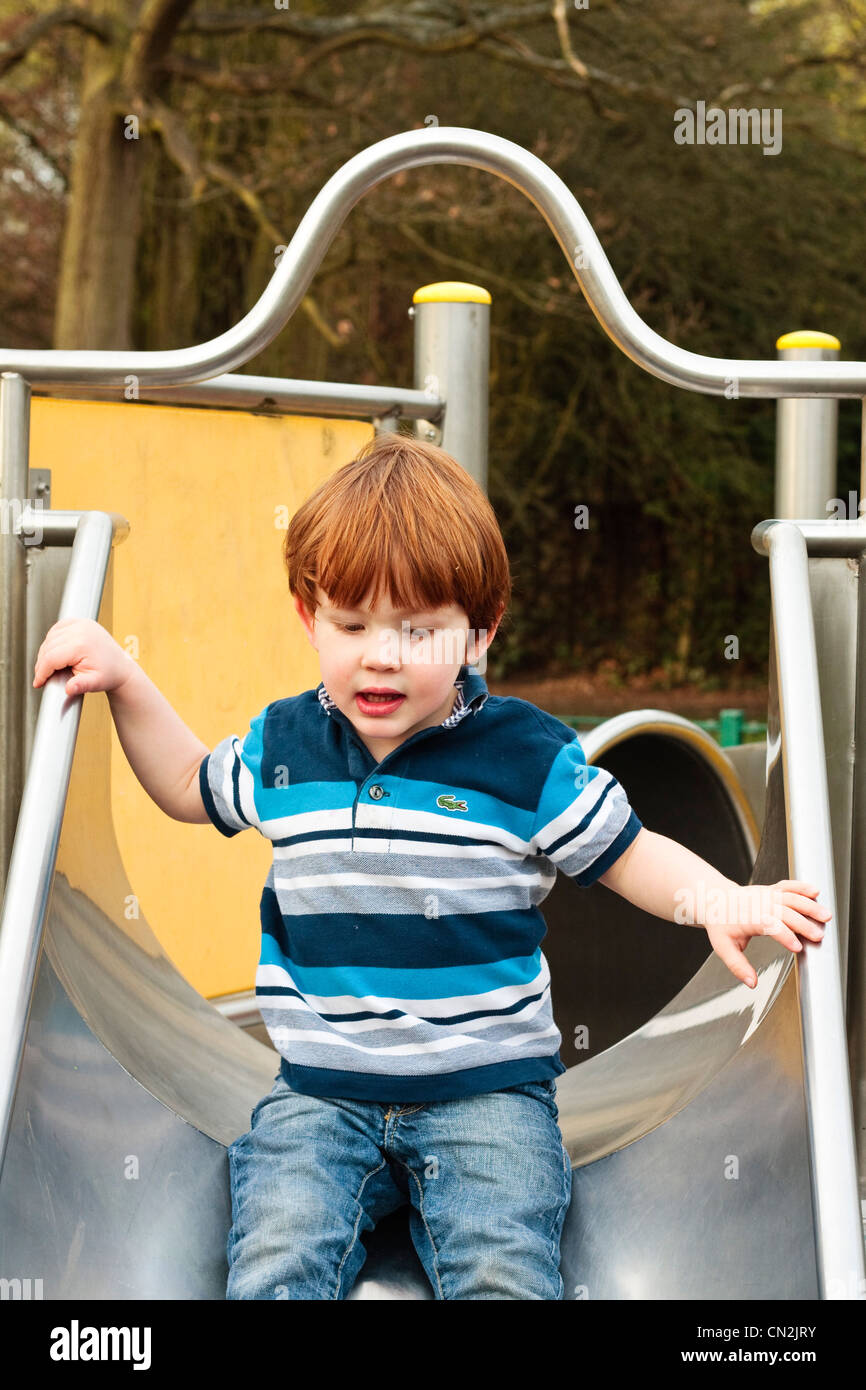 Portrait eines zwei Jahre alten Jungen hinunter eine Folie auf einem Spielplatz Stockfoto