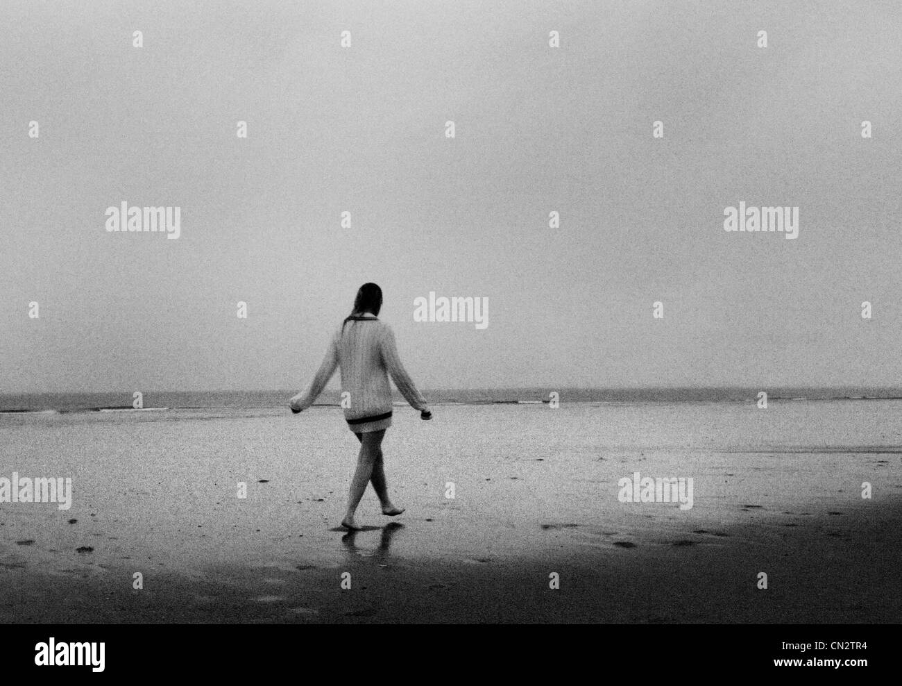 Junge Frau mit Pullover zu Fuß am Strand Stockfoto