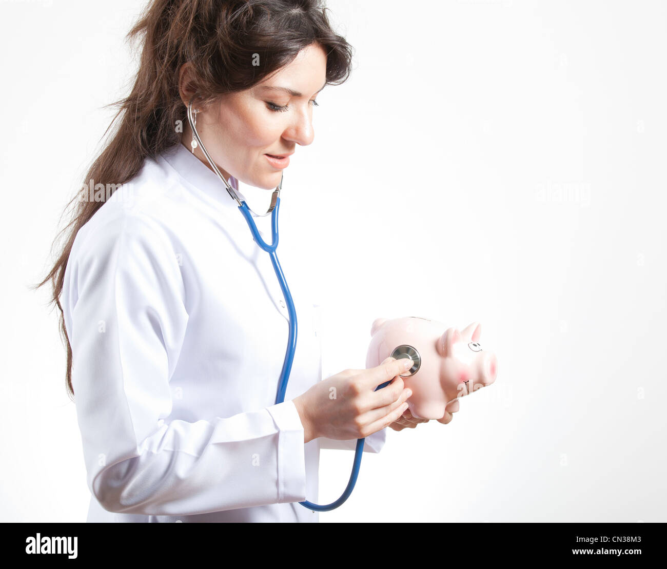 Frau Doktor Holding Stethoskop rosa Piggy Bank Stockfoto