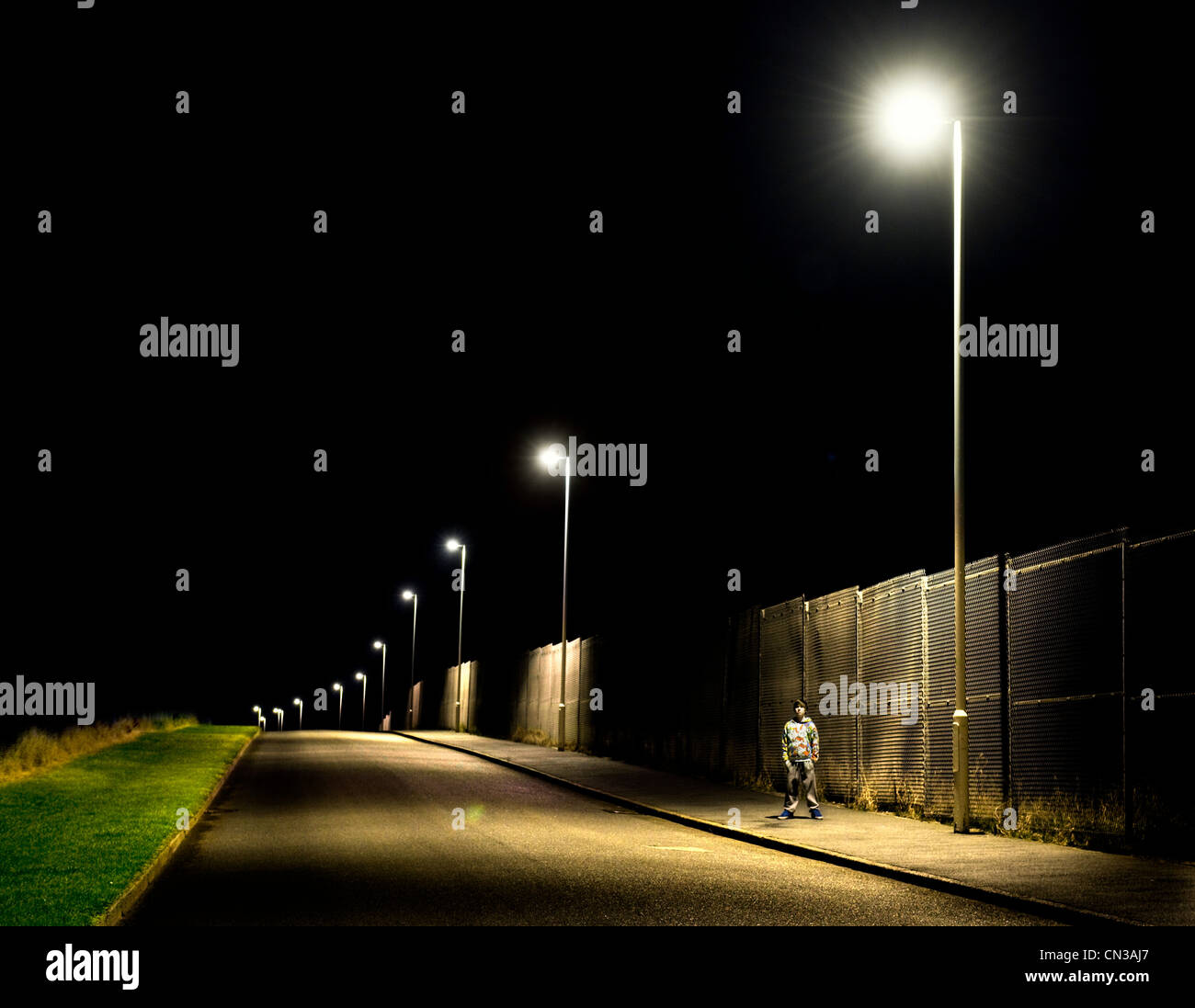 Junge stand auf Bürgersteig in der Nacht mit Straßenlaternen Stockfoto