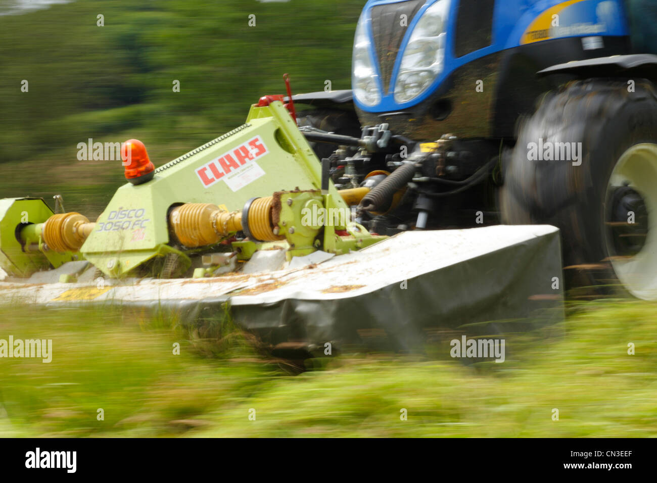 Auftragnehmer mit New Holland T6080 Traktor und Front montiert Claas Disco Rasenmäher mäht Rasen für die Silage. Stockfoto