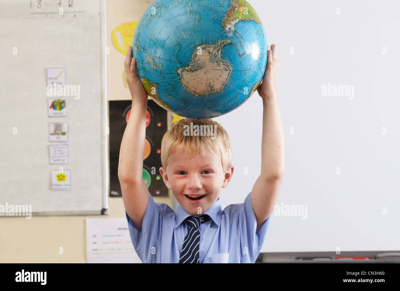 Schuljunge Globus über seinen Kopf in einem Klassenzimmer zu halten Stockfoto