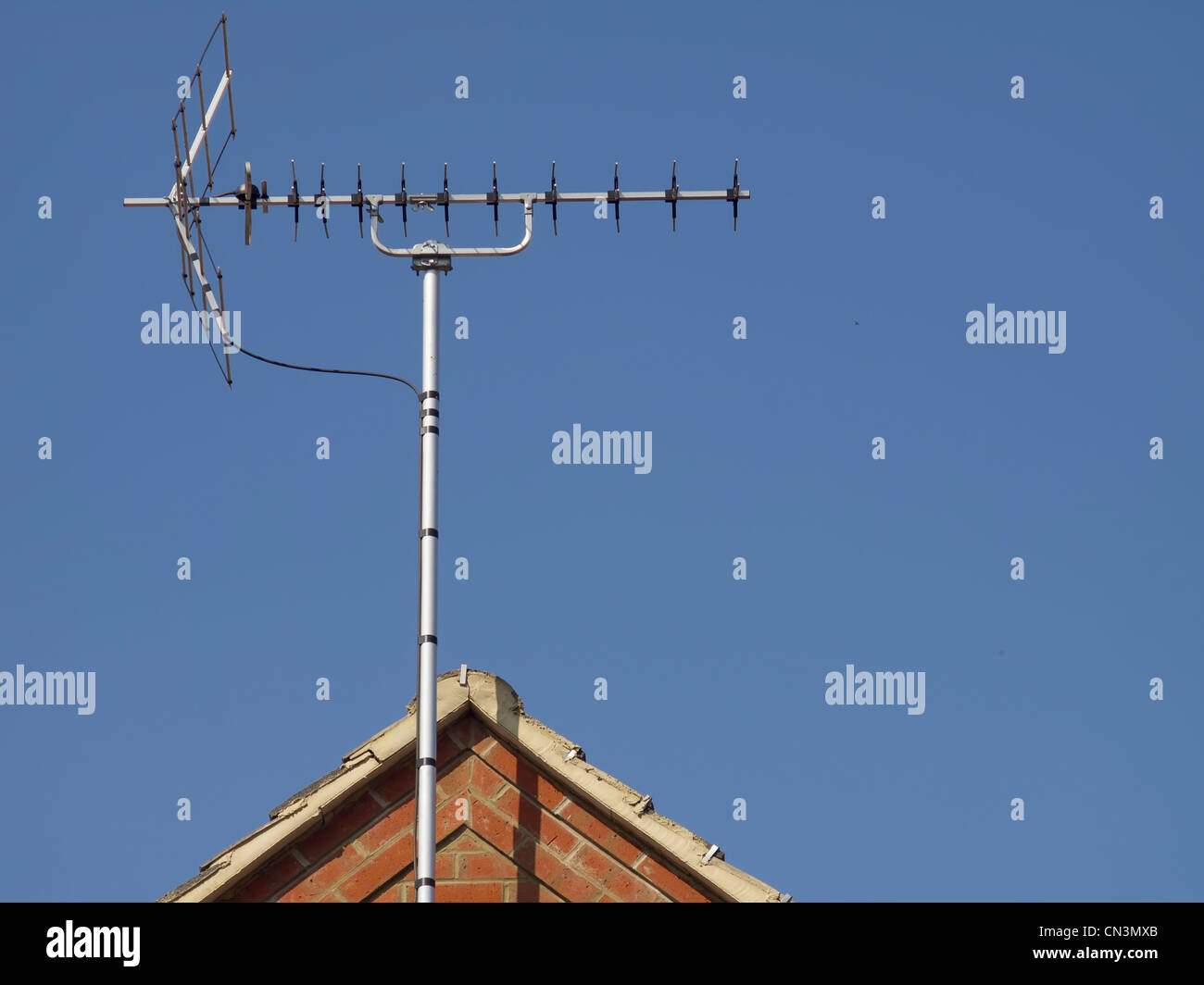 TV Antenne auf einem Hausdach, umrahmt von einem blauen Himmel. Stockfoto