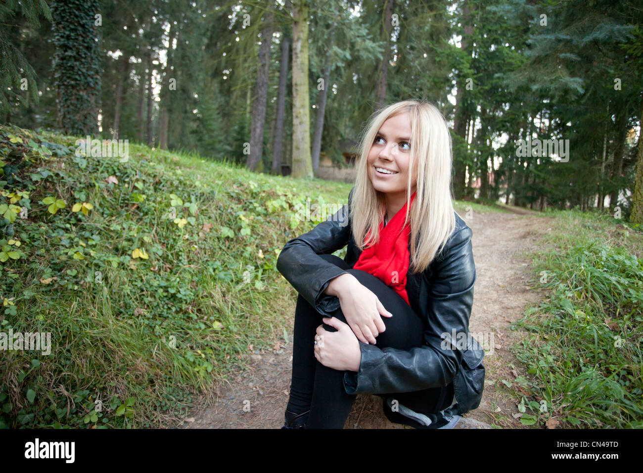 Lächelnde blonde Frau in Lederjacke sitzend Outdoorsю Stockfoto
