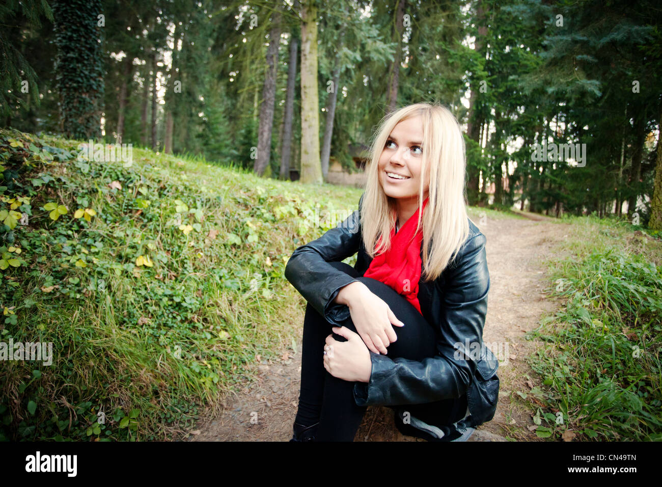 Lächelnde blonde Frau in Lederjacke sitzend Outdoorsю Stockfoto