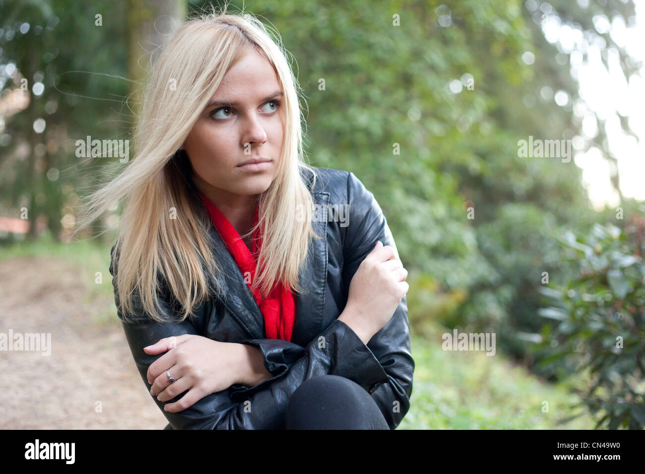 Nachdenkliche Frau in Lederjacke und rotem Schal draußen. Stockfoto