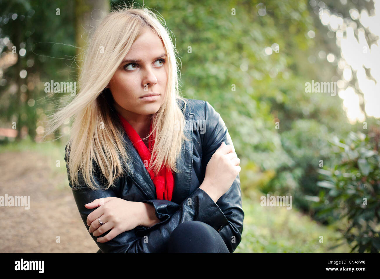 Nachdenkliche Frau in Lederjacke und rotem Schal draußen. Stockfoto