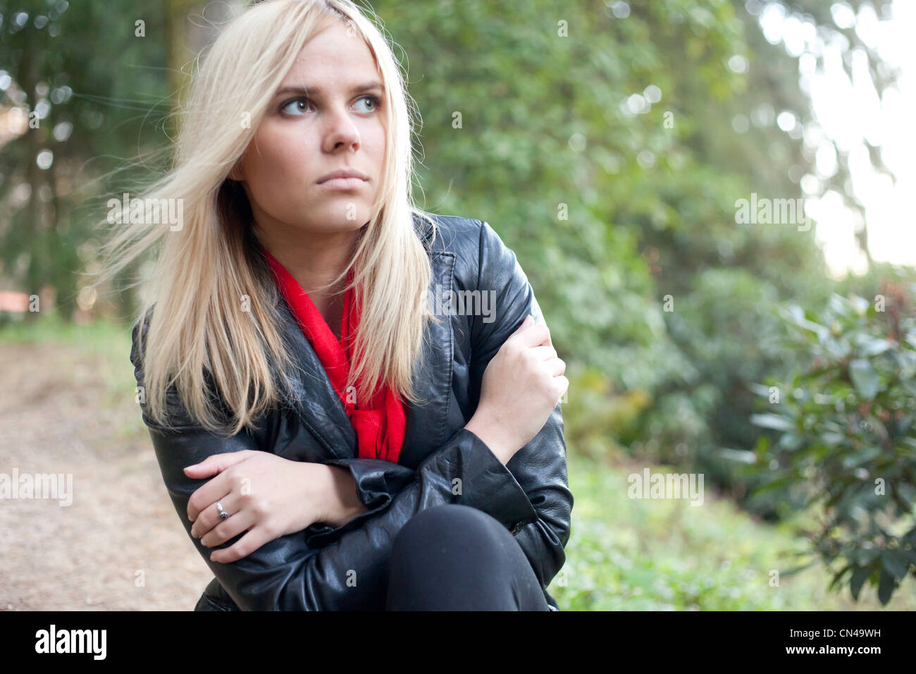 Nachdenkliche Frau in Lederjacke und rotem Schal draußen. Stockfoto