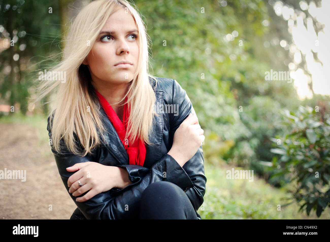Nachdenkliche Frau in Lederjacke und rotem Schal draußen. Stockfoto