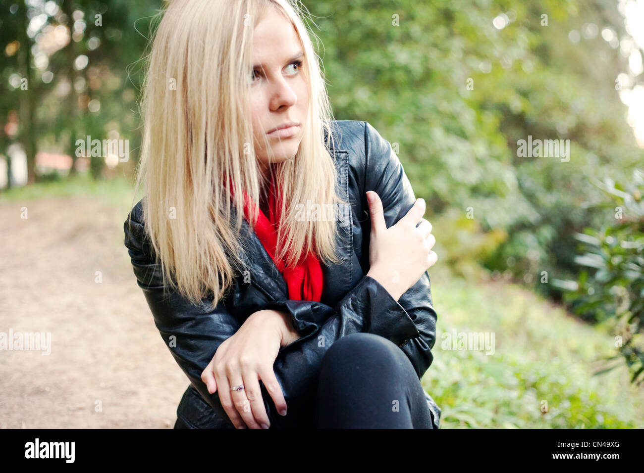 Nachdenkliche Frau in Lederjacke und rotem Schal draußen. Stockfoto