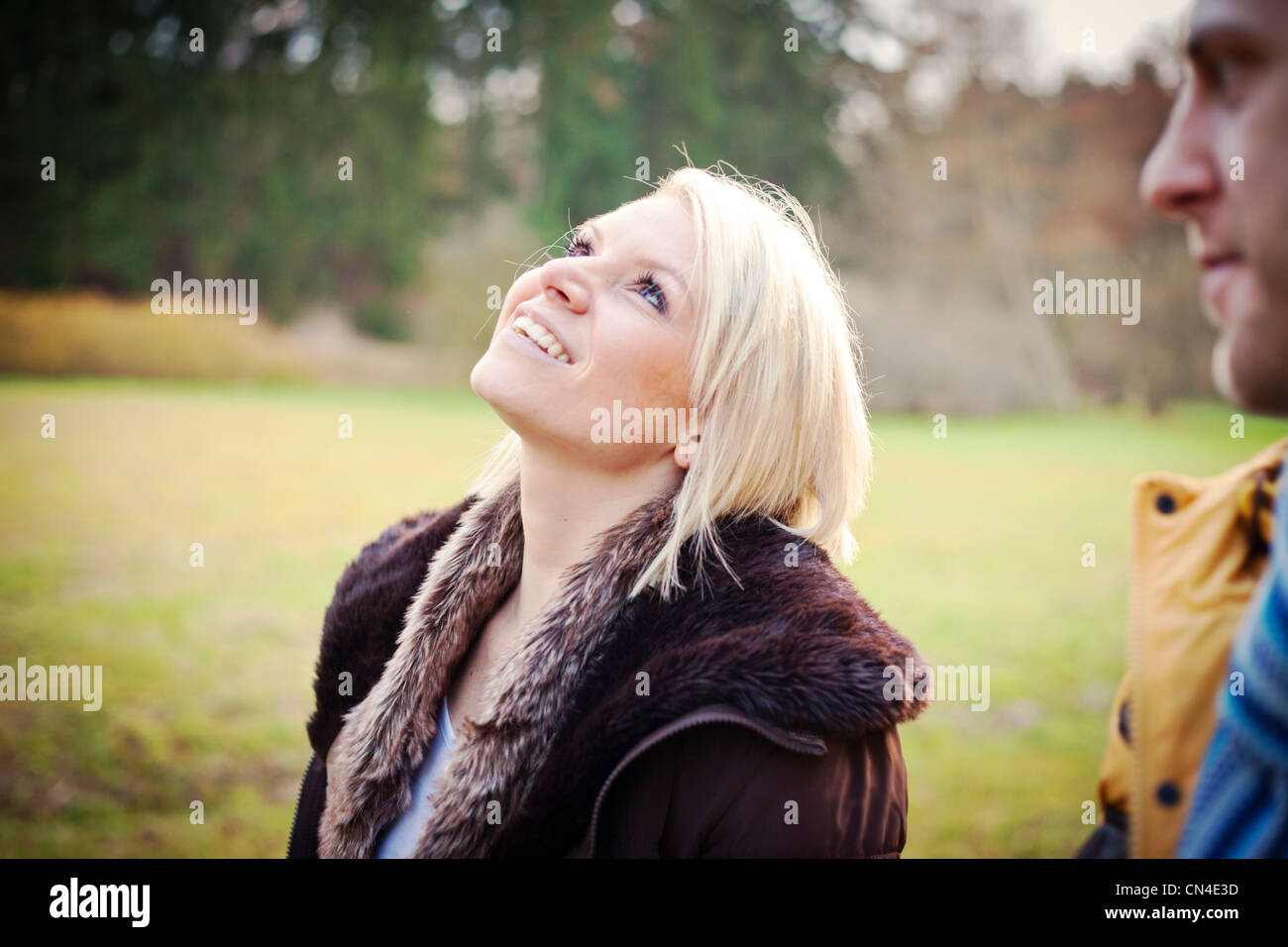 Fröhliche blonde Frau, die nach oben blickt mit einem lachenden Ausdruck, teilweise beschnittener Mann im Vordergrund Stockfoto
