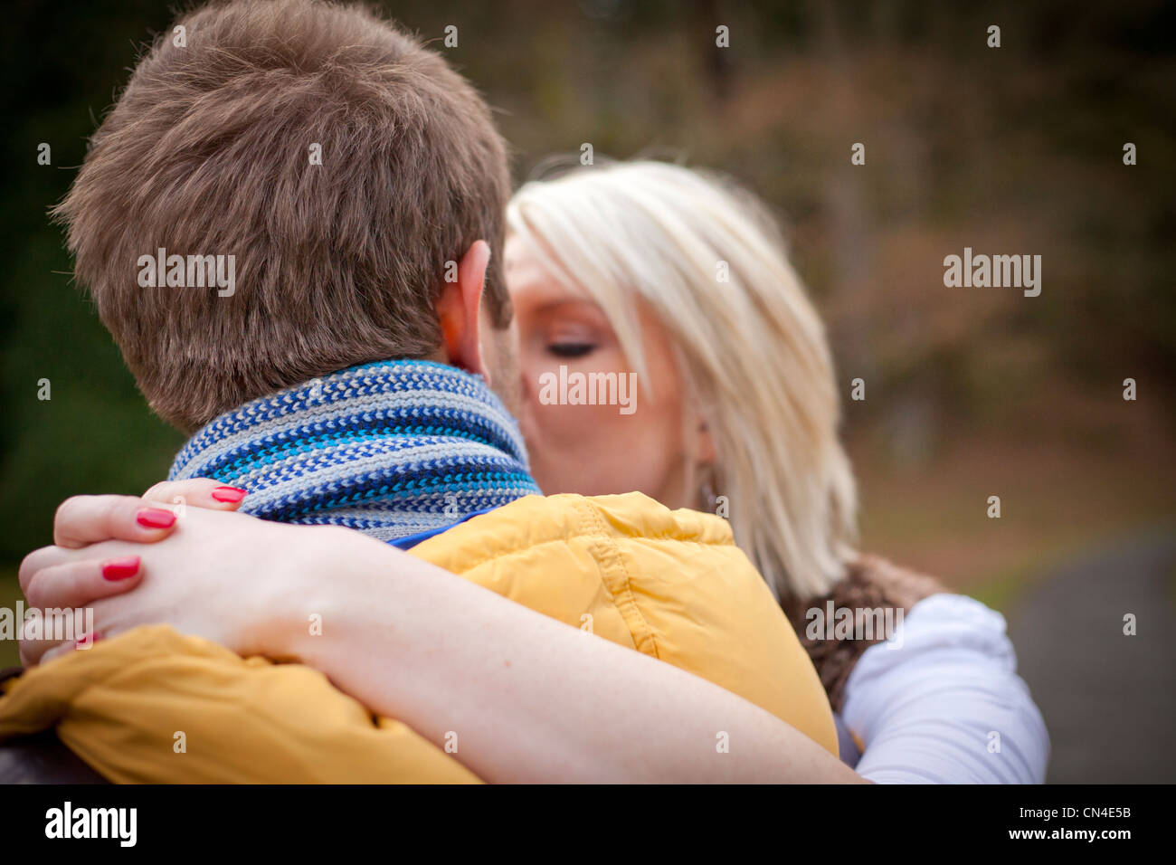 Nahaufnahme einer liebevollen Umarmung zwischen Mann und Frau, mit blondem Haar und roter Maniküre der Frau, während sie ihre Arme um ihn wickelt. Stockfoto