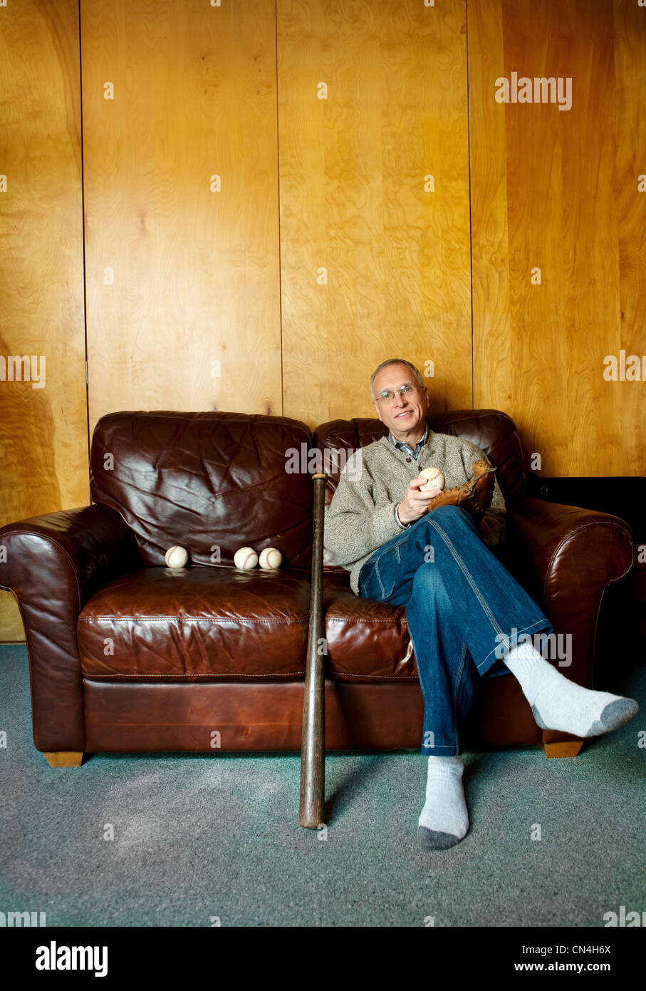 Senior Mann sitzt auf der Couch mit Baseballschläger Stockfoto