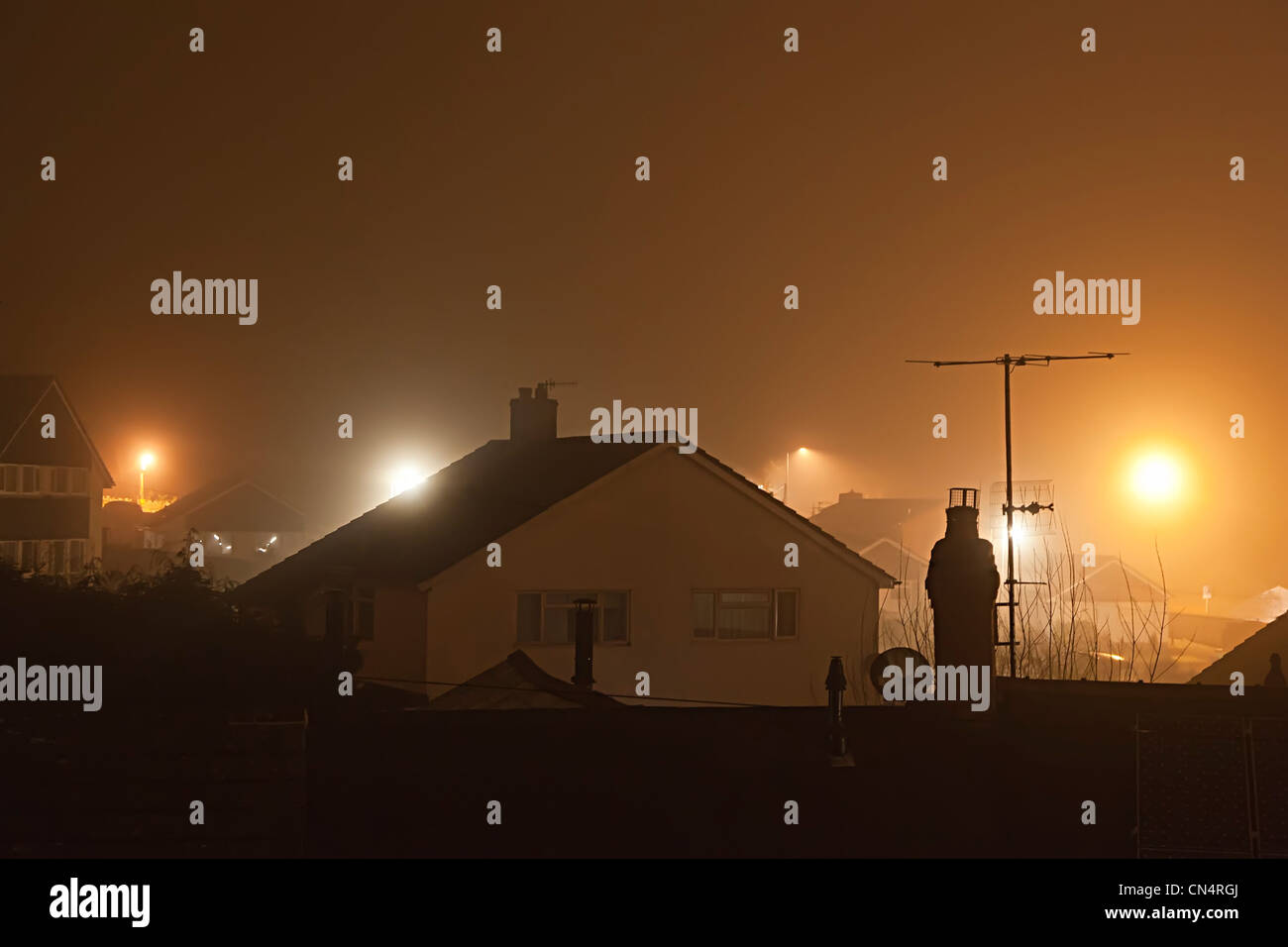 Häuser und Dächer in einer nebligen Nacht beleuchtet mit Straßenlaternen mit Lichtverschmutzung, Wales, UK Stockfoto