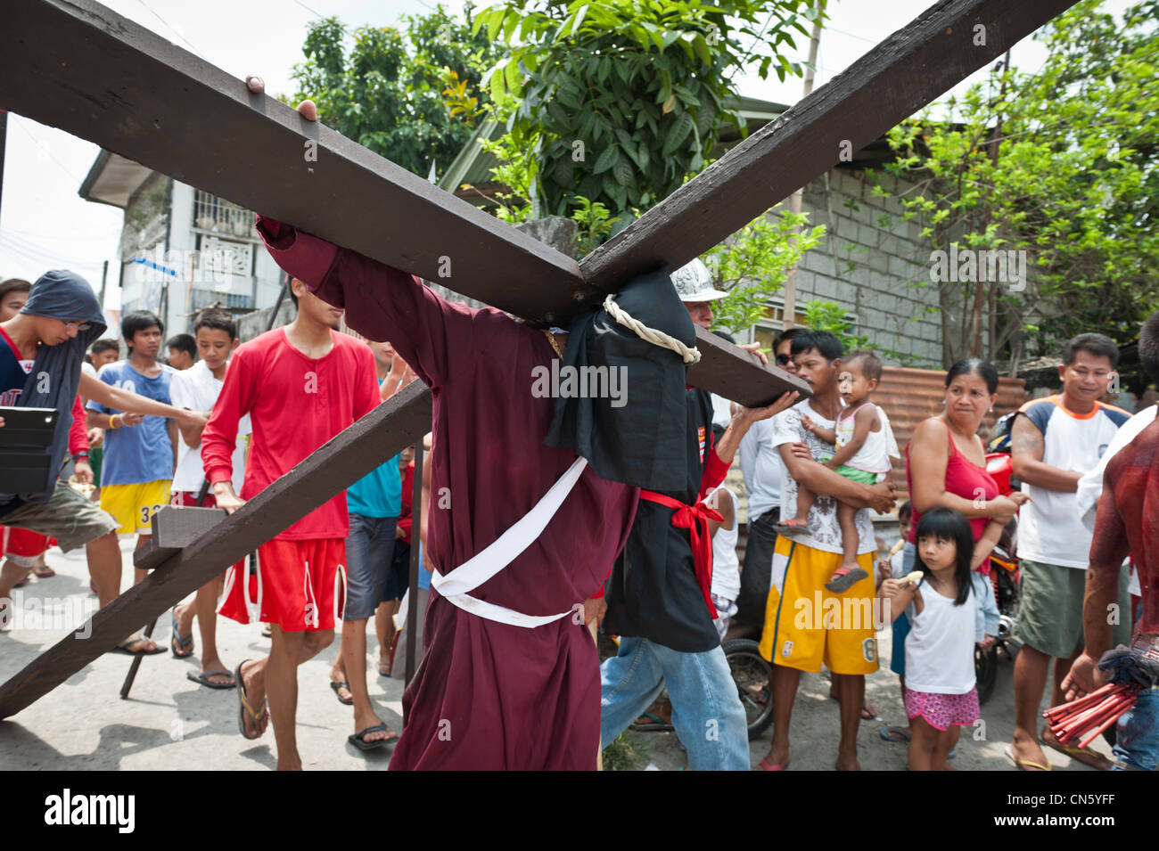 Maskierter Mann trägt ein Kreuz zu einem Standort der Kreuzigung am Karfreitag, San Fernando, Pampanga, Philippinen Stockfoto
