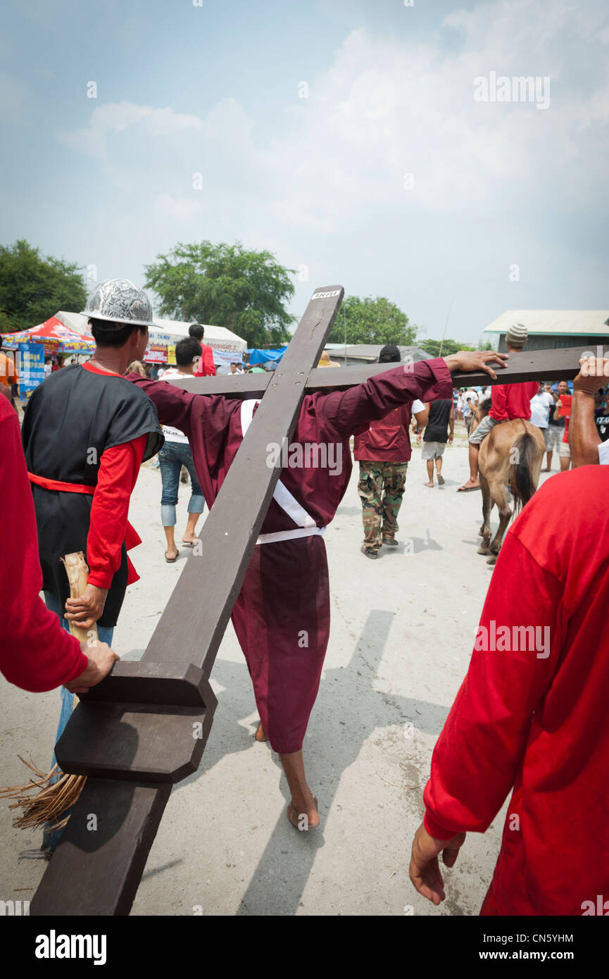 Maskierter Mann trägt ein Kreuz zu einem Standort der Kreuzigung am Karfreitag, San Fernando, Pampanga, Philippinen Stockfoto