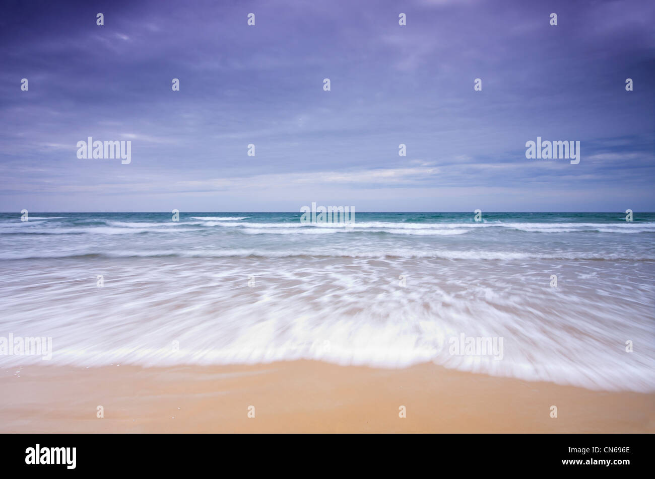 Welle mit Motion blur brechen am Sandstrand unter dunklem Himmel Stockfoto