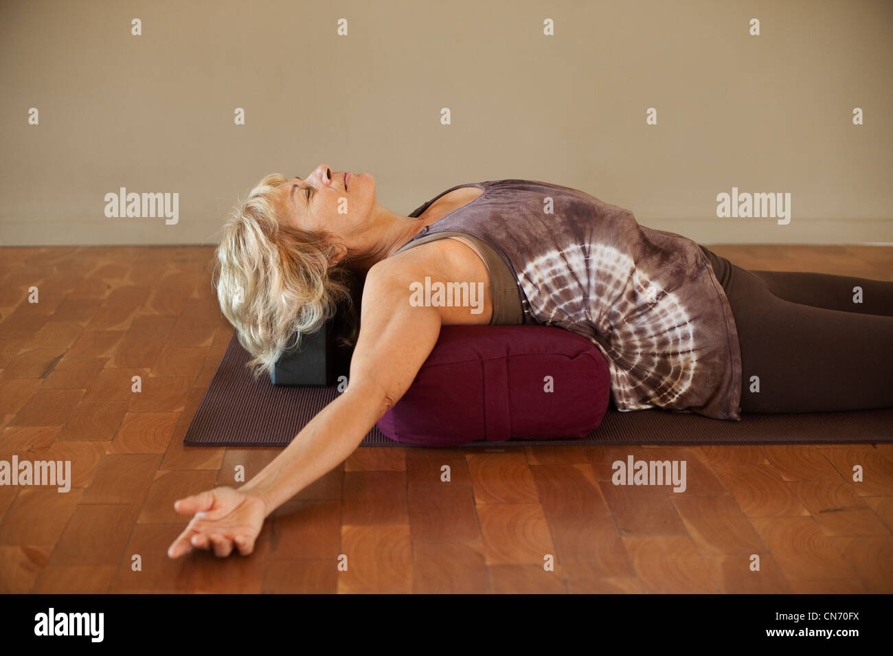 Mittleres Alter Frau ruht auf einem Yoga stärken. Restorative Yoga Asana Körperhaltung. Braun Tönen und tie dye Shirt. Stockfoto