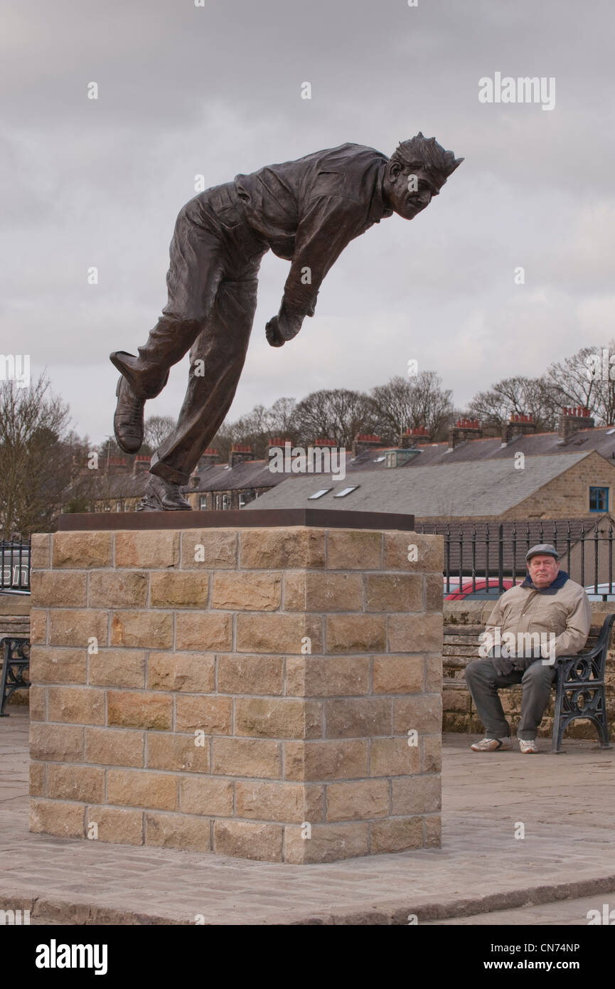 Mann sitzt auf der Bank, auf der Suche nach Bronze Statue der cricketer Fred (Freddie) Trueman (schnell Bower in Aktion) - Skipton, North Yorkshire, England, UK. Stockfoto