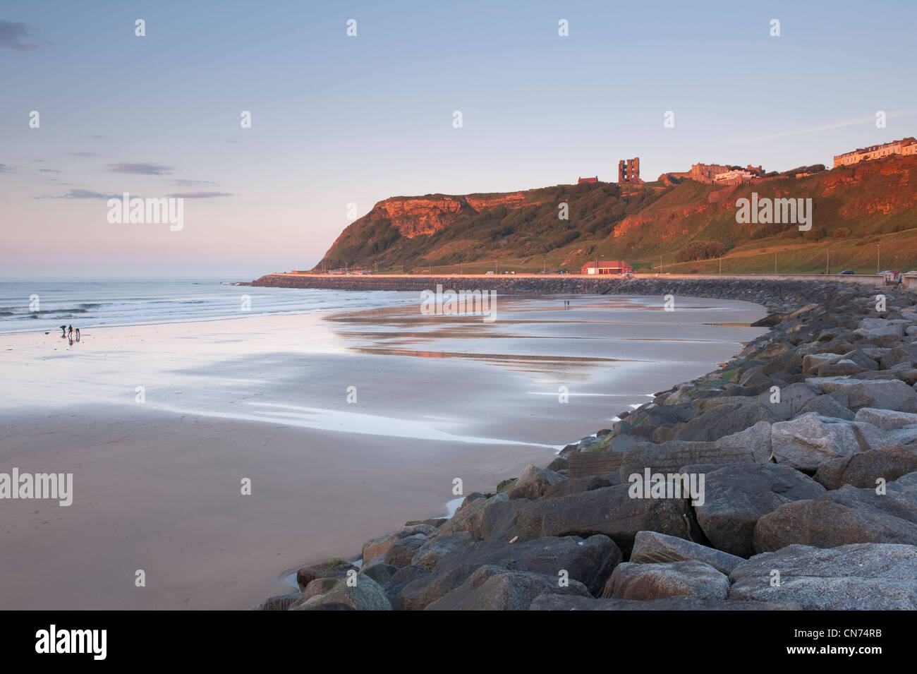 Malerische Ansicht des blauen Abendhimmel, glatt, flach, Sandstrand, ruhige See und sonnenbeschienene Schloss auf einer Klippe - North Bay, Scarborough, Yorkshire, England, UK. Stockfoto