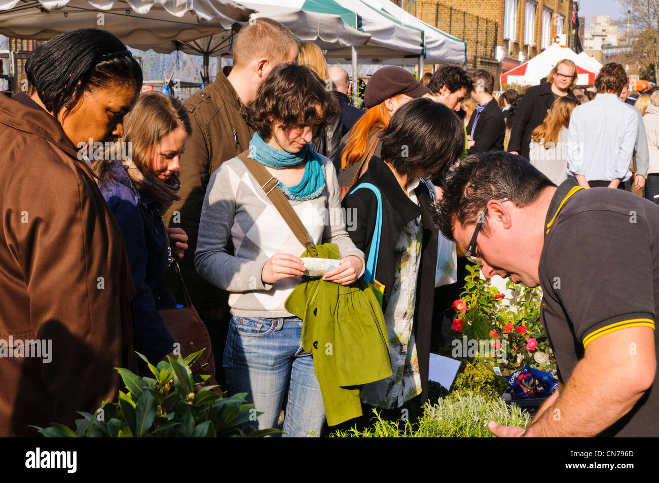 Eine junge Frau Kunde wartet halten Geld in der Hand an einem Stall in Sonntag Columbia Road Flower Market, East London, UK Stockfoto