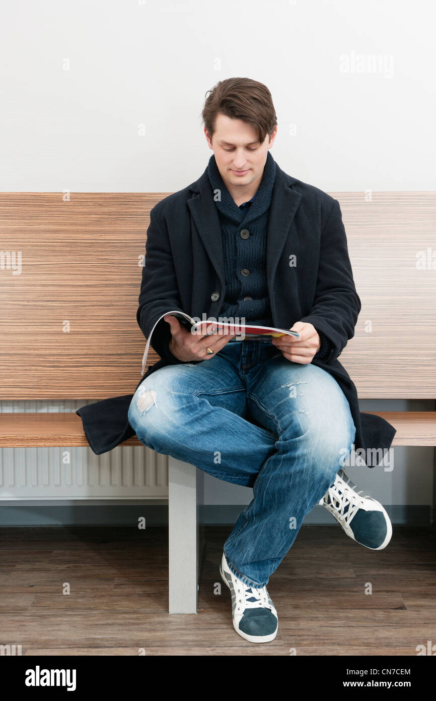Junger Mann sitzen im Wartezimmer eines Krankenhauses, einer Zeitschrift um die Zeit totzuschlagen Stockfoto