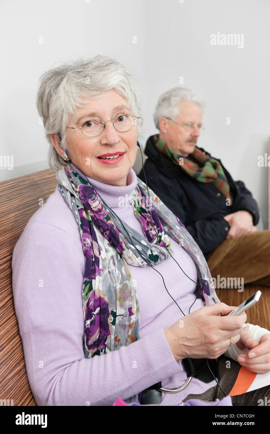 ältere Frau mit einem tragbaren MP3-Spieler sitzen auf einer Bank im Wartezimmer eines Krankenhauses Stockfoto